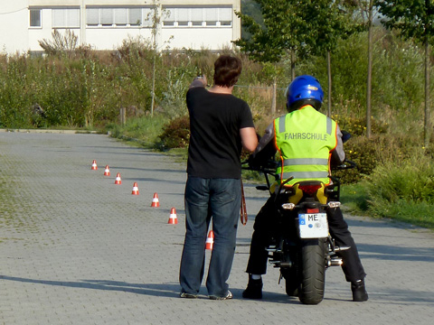 Bild vergrößern: Fahrlehrer erklrt seinem auf einem Motorrad sitzenden Fahrschler den vor sich liegenden Parkour.