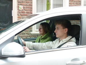 Bild vergrößern: Ein junger Erwachsener sitzt am Steuer eines Autos. Auf dem Beifahrersitz neben ihm sitzt eine ältere Dame.