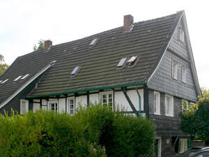 Bild vergrößern: Ein mit grüner Hecke umfasstes Fachwerkhaus.