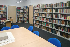 Bild vergrößern: Ein Raum mit vielen Bücherregalen entlang der Wände. Mittig steht ein Tisch mit Stühlen.