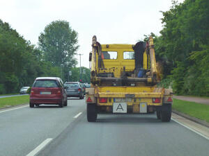 Bild vergrößern: Gelber Transporter für Container fährt auf einer Straße.