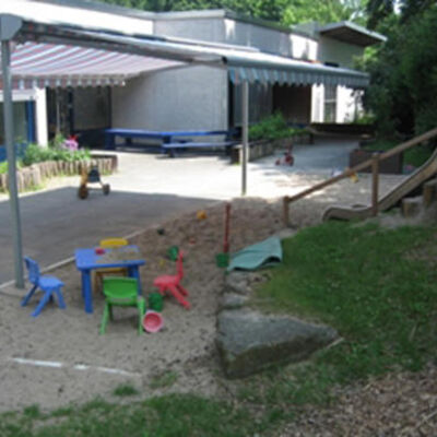 Bild vergrößern: Mit einem Sonnensegel berdachter Spielplatz mit im Sand liegendes Spielzeug.