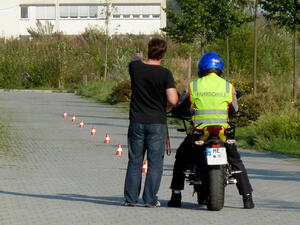 Bild vergrößern: Fahrlehrer erklärt seinem auf einem Motorrad sitzenden Fahrschüler den vor sich liegenden Parkour.