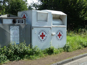 Bild vergrößern: Zwei weiße Altkleidercontainer des deutschen roten Kreuzes stehen neben einem Glascontainer.