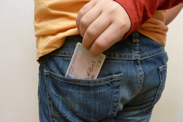 Bild vergrößern: Eine Hand greift einen Fhrerschein aus der hinteren Hosentasche einer vor sich stehenden Person.
