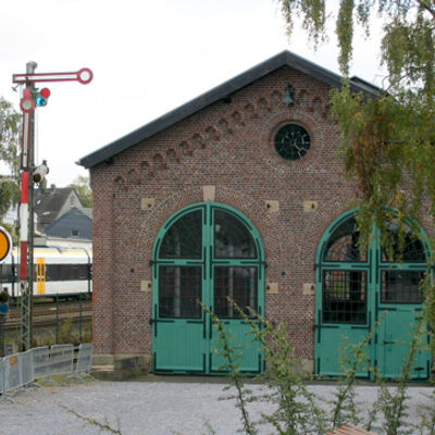 Bild vergrößern: Altes Bahngebäude, daneben eine Signalsäule.