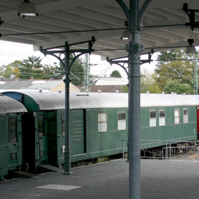 Bild vergrößern: Grüne Eisenbahnwaggons stehen an einem überdachten Bahnsteig.