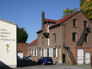 Bild vergrößern: Rotes Backsteingebäude, daneben ein weiteres Gebäude mit einem Verweis auf die Website des Wilhelm-Fabry-Museums.