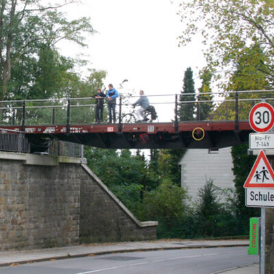 Bild vergrößern: Auf einer Radwegbrücke befinden sich zwei Personen und ein Radfahrender.