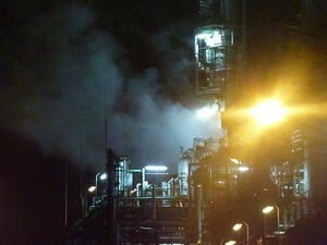 Bild vergrößern: Nächtliches Fabrikgelände mit ausstoßenden Rauch.