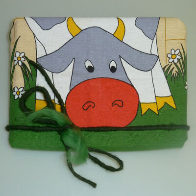 Bild vergrößern: Ein mit einem Küchentuch verpacktes Geschenk mit dem Motiv einer auf einer Wiese grasenden Kuh.