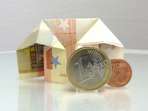 Bild vergrößern: Eine 1-Euro und eine 1-Cent Münze stehen vor einem zum Haus gefalteten Geldschein.