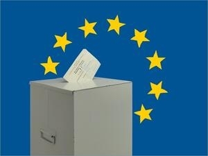 Bild vergrößern: Ein Stimmzettel steckt im Schlitz einer Wahlurne. Im Hintergrund befindet sich das Logo der Europäischen Union.