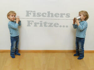 Bild vergrößern: Zwei Kinder unterhalten sich über ein Dosentelefon, an dessen Schnur die Worte "Fischers Fritze" stehen.