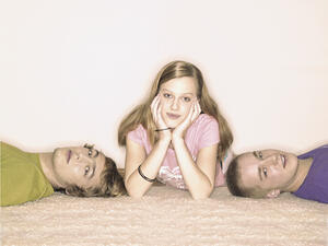 Bild vergrößern: Drei Schulkinder liegen auf einem Boden.