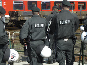 Bild vergrößern: Polizisten in Schutzausrüstung stehen an einem Bahngleis.
