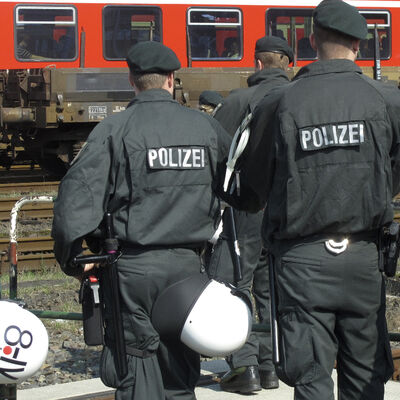 Bild vergrößern: Polizisten in Schutzausrstung stehen an einem Bahngleis.