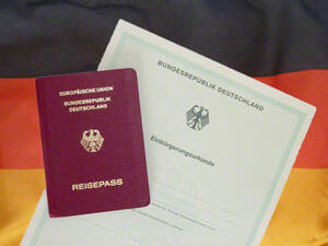 Bild vergrößern: Einbürgerungsurkunde der Bundesrepublik Deutschland und ein deutscher Reisepass liegen auf einer Deutschlandflagge.