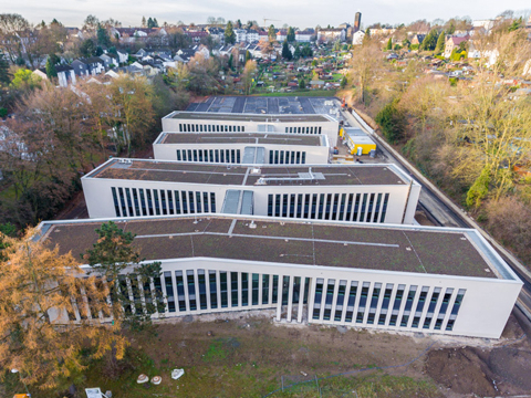 Bild vergrößern: Von oben gerichtete Ansicht auf vier hintereinander gereihte längliche Gebäudekomplexe.