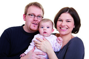 Bild vergrößern: Ein Elternpaar halten ihr Kleinkind auf den Armen.