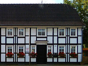 Bild vergrößern: Ein Fachwerkhaus mit roten Blumen auf den Fensterbänken, neben der Haustür hängt ein Schild mit dem Logo der AWO in Langenfeld.