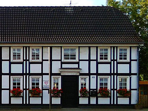 Bild vergrößern: Ein Fachwerkhaus mit roten Blumen auf den Fensterbnken, neben der Haustr hngt ein Schild mit dem Logo der AWO in Langenfeld.