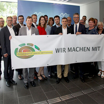 Bild vergrößern: Gruppe von Personen halten einen Banner mit der Aufschrift: "Wir machen mit" und dem Logo: "Ökoprofit Kreis Mettmann" vor sich.