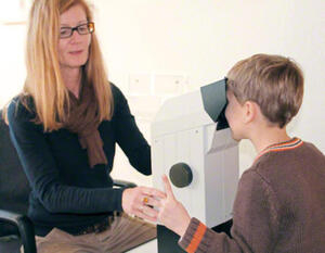Bild vergrößern: Eine Frau untersucht einen an einem Augengerät stehenden Jungen.