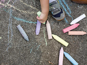 Bild vergrößern: Eine Kinderhand malt mit Kreide auf dem Boden.