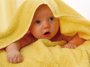 Bild vergrößern: Baby eingewickelt in einem gelben Handtuch.