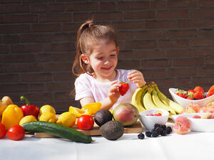 Bild vergrößern: Ein kleines Mädchen sitzt an einem mit einer Vielzahl an verschiedenen Obstsorten gedeckten Tisch.