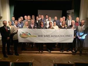Bild vergrößern: Eine Gruppe von Personen halten einen weißen Banner mit der Aufschrift: "Wir sind ausgezeichnet" und dem Logo des ÖKOPROFIT Kreis Mettmann.