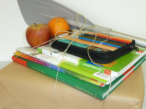 Bild vergrößern: Schulmaterialien und Obst sind zu einem Paket zusammengeschnürt.