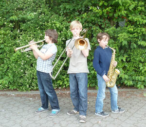 Bild vergrößern: Drei Kinder spielen stehend Trompete, Posaune und Saxofon.