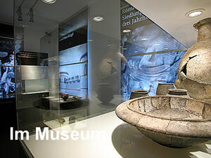 Bild vergrößern: Eine Waschschüssel und ein Krug, im Hintergrund sind Informationstafeln zum Haus Bürgel und zu alten Römerhaussiedlungen.