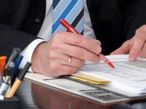 Bild vergrößern: Eine Hand mit Kugelschreiber kontrolliert Unterlagen in einem Ordner.