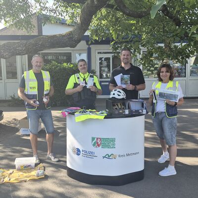 Bild vergr&ouml;&szlig;ern: Vier Personen pr&auml;sentieren Fahrrad-Sicherheitsausr&uuml;stung an einem Informationsstand im Freien.
