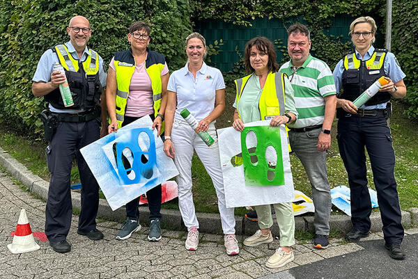 Bild vergrößern: Gruppenbild von einer Aktion bei der Fußspuren als Markierung auf die Straße gesprayt wurden zum Thema "Wir wollen gehen! Zu Fuß statt Elterntaxi".